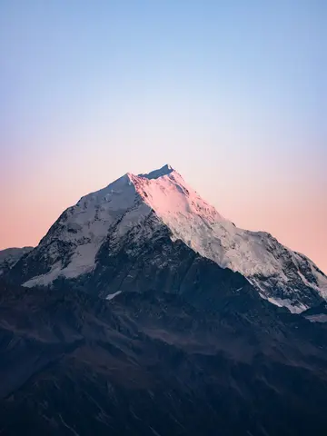 Snow-capped mountain peak at sunrise with pastel sky